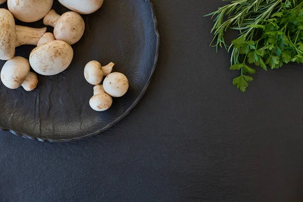 Yeşillikleri ile siyah bir tabakta champignon mantar