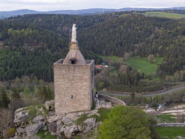 Luc Kalesi 'nin taş kulesi. Fransa' nın Lozere bölgesindeki yemyeşil vadi, orman ve dolambaçlı yola bakıyor.
