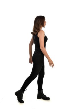 Tam boy siyah singlet, kot kot pantolon ve bot giyen esmer kız portresi. ayakta poz, uzak kameradan karşı karşıya. beyaz stüdyo arka plan üzerinde izole.