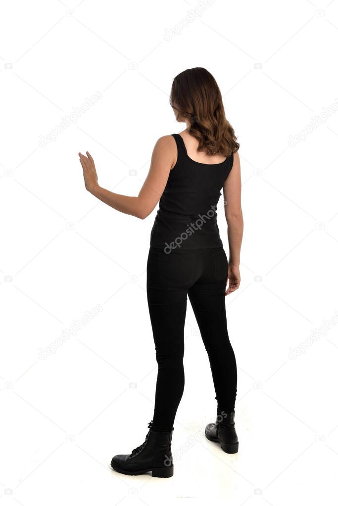 full length portrait of brunette girl wearing black singlet, jeans jeans and boots. standing pose, facing away from the camera. isolated on white studio background.