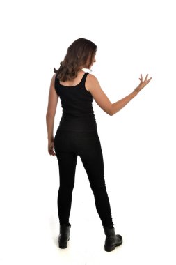 Tam boy siyah singlet, kot kot pantolon ve bot giyen esmer kız portresi. ayakta poz, uzak kameradan karşı karşıya. beyaz stüdyo arka plan üzerinde izole.