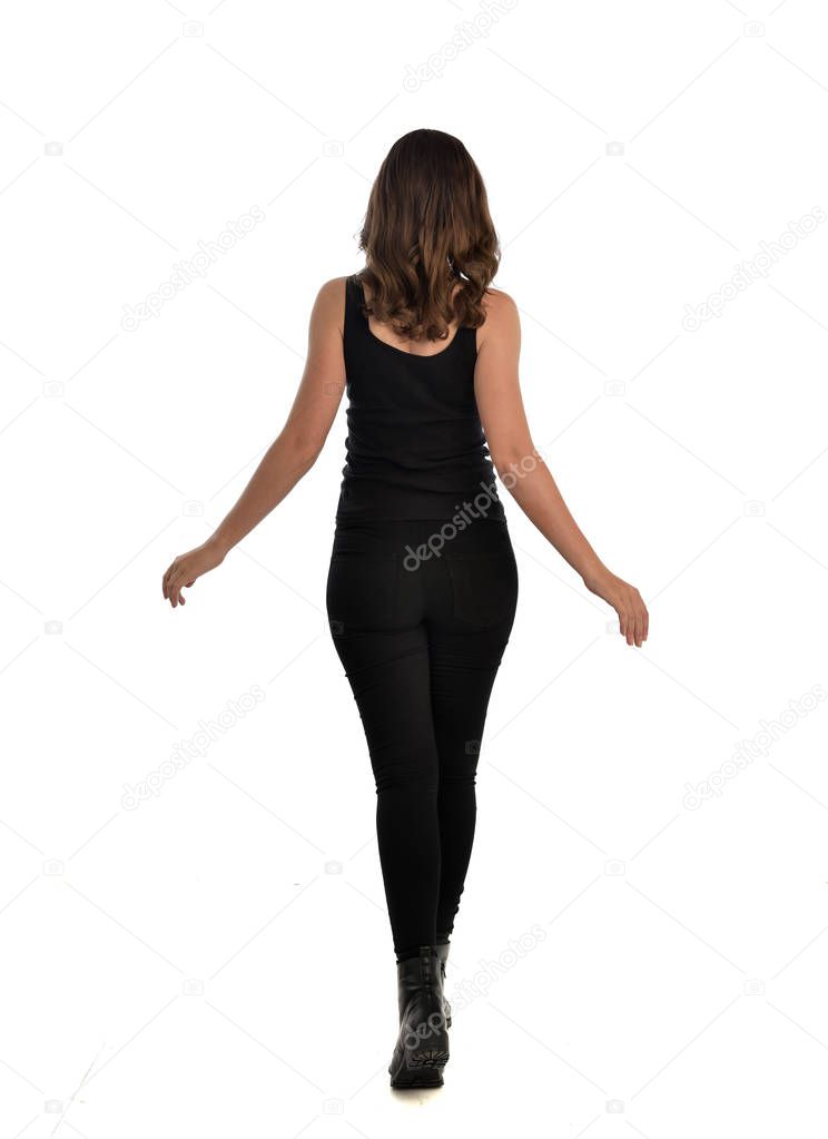 full length portrait of brunette girl wearing black singlet, jeans jeans and boots. standing pose, facing away from the camera. isolated on white studio background.