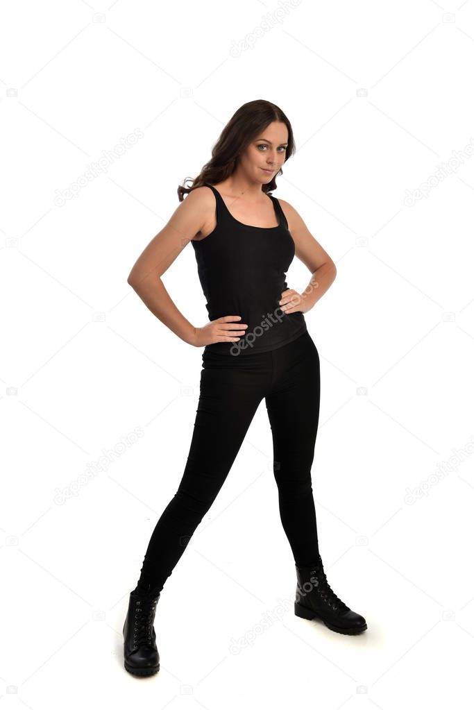 full length portrait of brunette girl wearing black singlet, jeans jeans and boots. standing pose, isolated on white studio background.