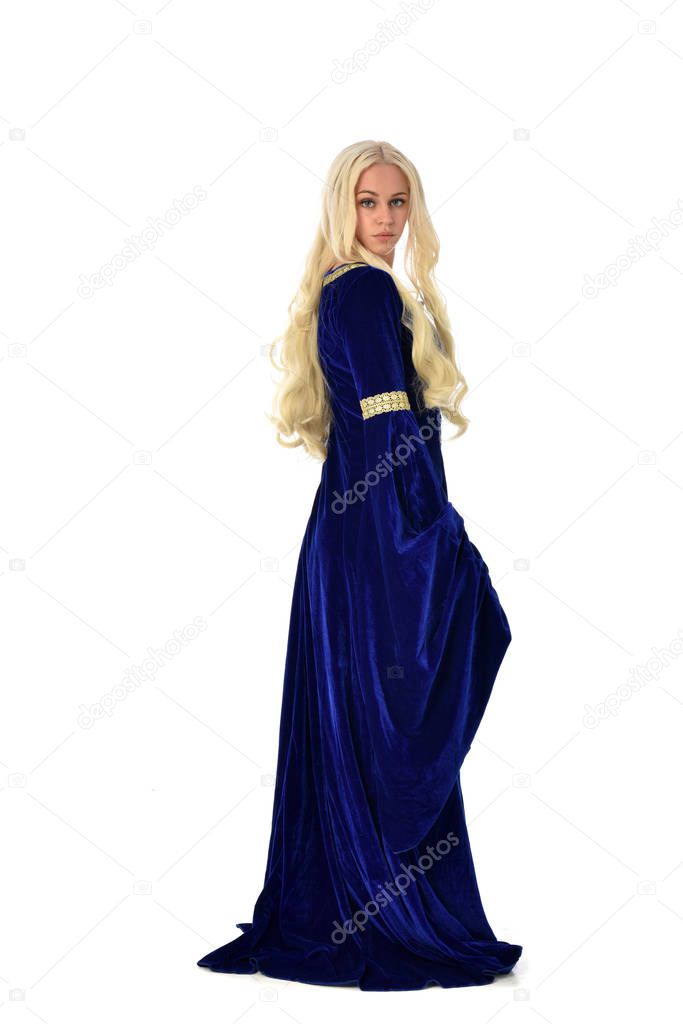 full length portrait of pretty blonde lady wearing  a blue fantasy medieval gown. standing pose  facing away from the camera, on white studio background.