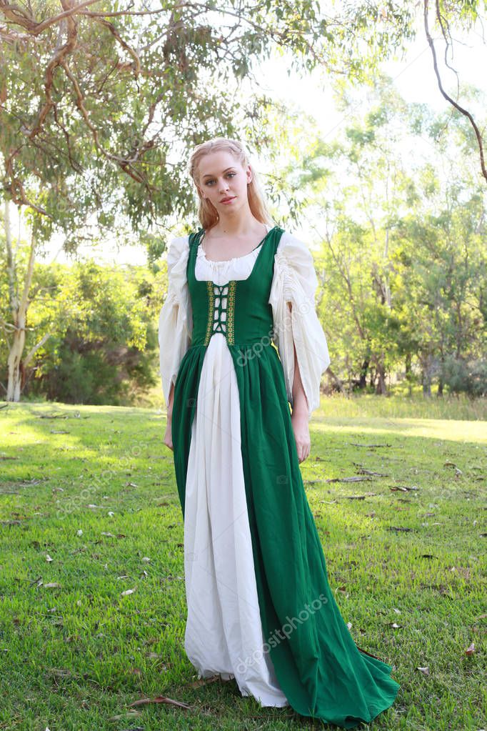 full length portrait of blonde woman wearing green medieval gown, wandering through a forest.