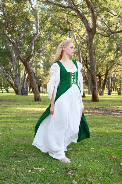 full length portrait of blonde woman wearing green medieval gown, wandering through a forest.