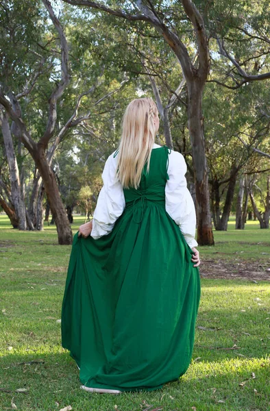 full length portrait of blonde woman wearing green medieval gown, wandering through a forest.