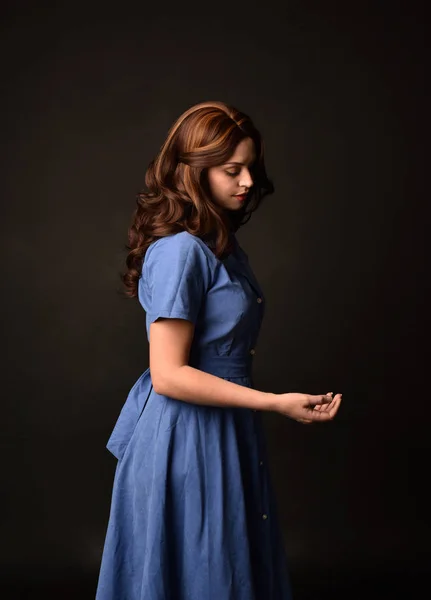 青いドレスを着ているブルネットの女性の肖像画 黒のスタジオの背景にカメラに戻るとポーズ — ストック写真