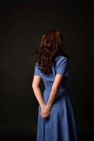 青いドレスを着ているブルネットの女性の肖像画 黒のスタジオの背景にカメラに戻るとポーズ — ストック写真