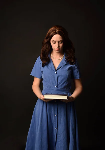 青いドレスを着て 本を持ってブルネットの女性の肖像画 黒のスタジオの背景にもたらされる — ストック写真