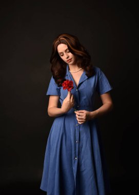 3/4 mavi elbise, bir çiçek tutan esmer Bayan portresi. siyah stüdyo arka plan üzerinde poz verdi.