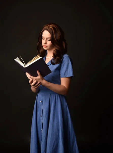 青いドレスを着て 本を持ってブルネットの女性の肖像画 黒のスタジオの背景にもたらされる — ストック写真