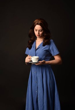 3/4 mavi elbise, bir çay bardağı tutan esmer Bayan portresi. siyah stüdyo arka plan üzerinde poz verdi.