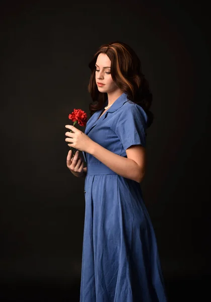 青いドレスを着て 花を持ってブルネットの女性の肖像画 黒のスタジオの背景にもたらされる — ストック写真