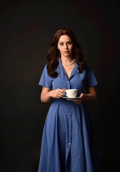 青いドレスを着て 紅茶のカップを持ってブルネットの女性の肖像画 黒のスタジオの背景にもたらされる — ストック写真