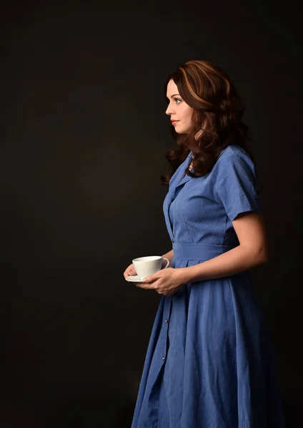 青いドレスを着て 紅茶のカップを持ってブルネットの女性の肖像画 黒のスタジオの背景にもたらされる — ストック写真