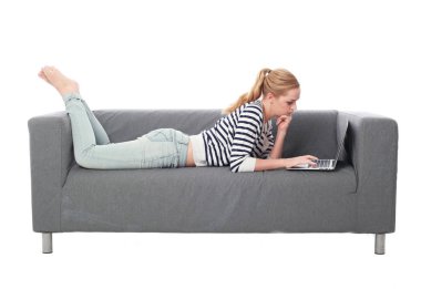 beyaz stüdyo arka plan üzerinde izole bir gri kanepede oturan kız portresi tam uzunlukta.