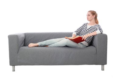 beyaz stüdyo arka plan üzerinde izole bir gri kanepede oturan kız portresi tam uzunlukta.