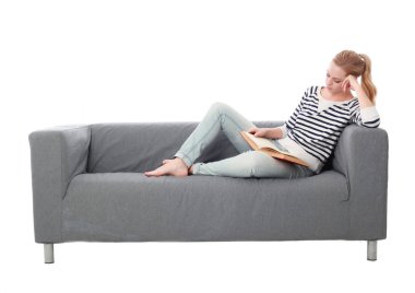 beyaz stüdyo arka plan üzerinde izole bir gri kanepede oturan kız portresi tam uzunlukta.