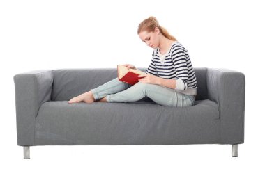 beyaz stüdyo arka plan üzerinde izole bir gri kanepede oturan kız portresi tam uzunlukta.