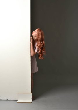Mor yazlık elbise giyiyor, bir duvara yaslanmış bir kız, tam uzunlukta portresi. gri studio arka plan.