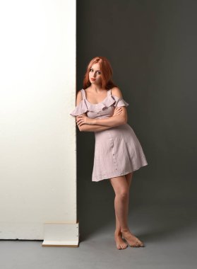 Mor yazlık elbise giyiyor, bir duvara yaslanmış bir kız, tam uzunlukta portresi. gri studio arka plan.