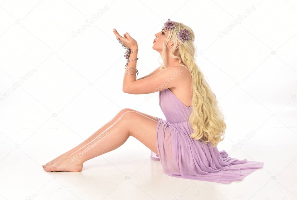 full length portrait of blonde girl in purple dress, seated pose on white studio background.