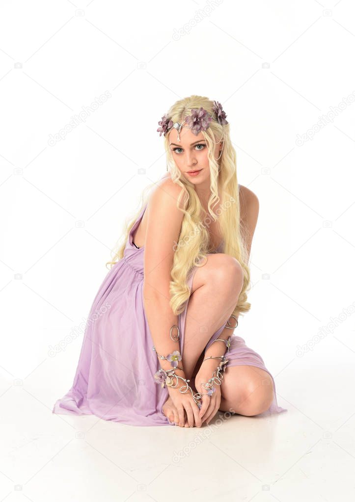 full length portrait of blonde girl in purple dress, seated pose on white studio background.