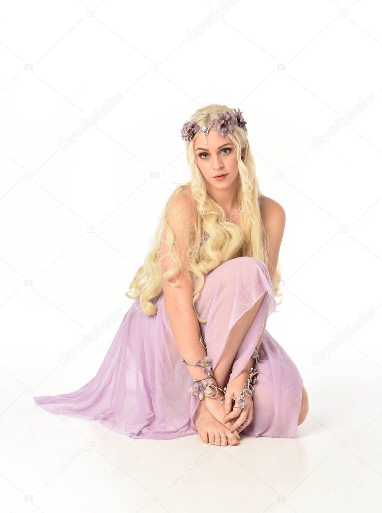 full length portrait of blonde girl in purple dress, seated pose on white studio background.