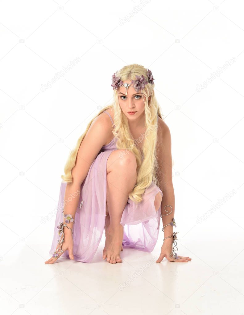 full length portrait of blonde girl in purple dress, seated pose on white studio background.