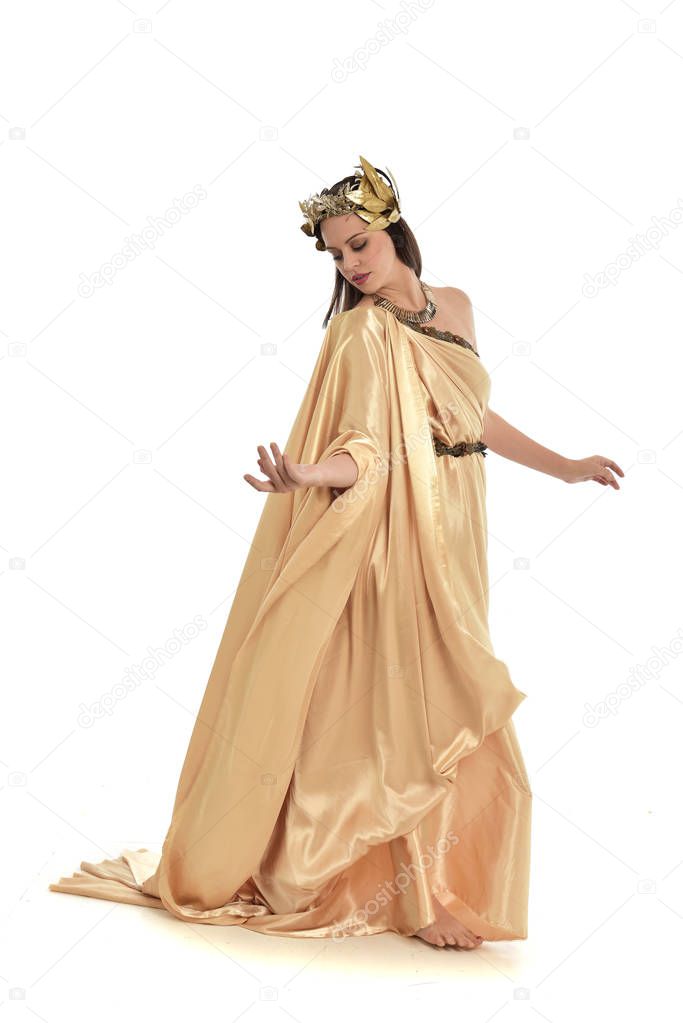 full length portrait of brunette woman wearing gold grecian gown, standing pose. isolated on white studio background.
