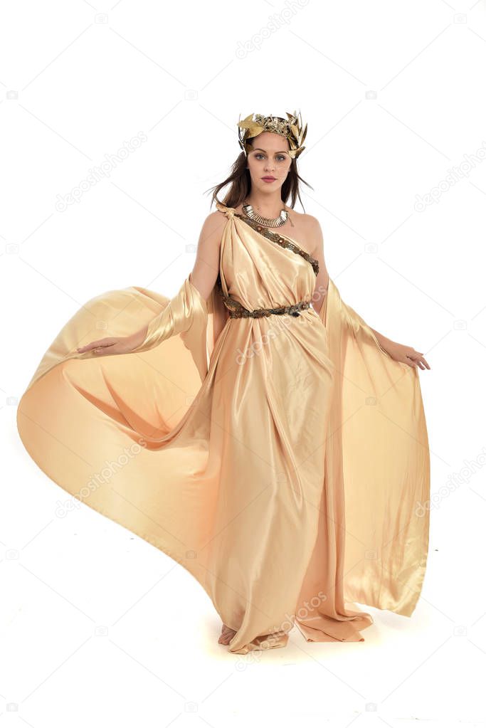 full length portrait of brunette woman wearing gold grecian gown, standing pose. isolated on white studio background.