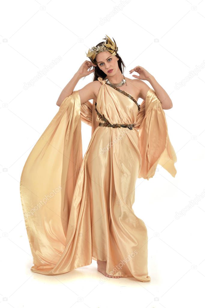 full length portrait of brunette woman wearing gold grecian gown, standing pose. isolated on white studio background.