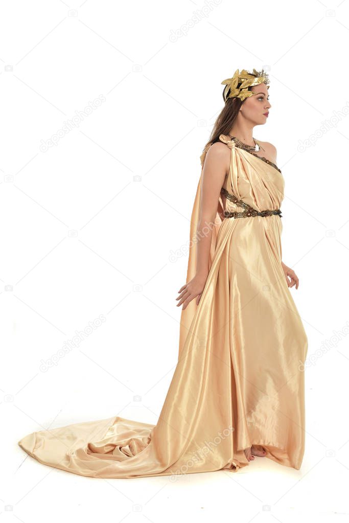 full length portrait of brunette woman wearing gold grecian gown, standing pose. isolated on white studio background.