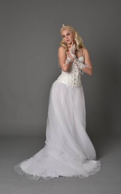 tam uzunlukta portre sarışın kız beyaz korse elbisesi giyiyor. gri studio arka plan üzerinde ayakta poz.