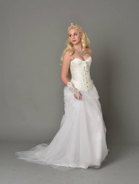 tam uzunlukta portre sarışın kız beyaz korse elbisesi giyiyor. gri studio arka plan üzerinde ayakta poz.