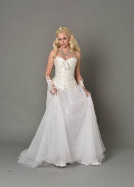 tam uzunlukta portre sarışın kız beyaz korse elbisesi giyiyor. gri studio arka plan üzerinde ayakta poz.