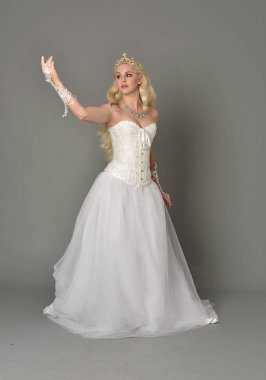 tam uzunlukta portre sarışın kız beyaz korse elbisesi giyiyor. gri studio arka plan üzerinde ayakta poz.