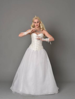 tam uzunlukta portre sarışın kız beyaz korse elbisesi giyiyor. gri studio arka plan üzerinde ayakta poz.