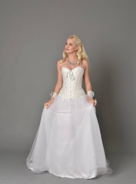 tam uzunlukta portre sarışın kız beyaz korse elbisesi giyiyor. gri studio arka plan üzerinde ayakta poz.