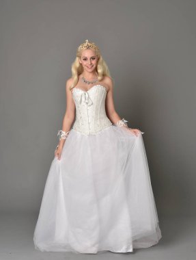 tam uzunlukta portre sarışın kız beyaz korse elbisesi giyiyor. gri studio arka plan üzerinde ayakta poz.