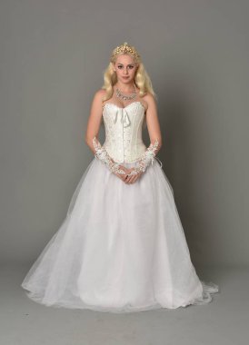 tam uzunlukta portre sarışın kız beyaz korse elbisesi giyiyor. gri studio arka plan üzerinde ayakta poz.