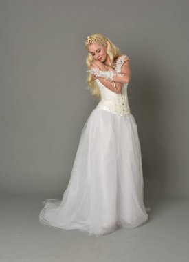 tam uzunlukta portre sarışın kız beyaz korse elbisesi giyiyor. gri studio arka plan üzerinde ayakta poz.