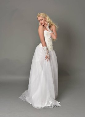 tam uzunlukta portre sarışın kız beyaz korse elbisesi giyiyor. gri studio arka plan üzerinde ayakta poz.