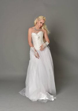 tam uzunlukta portre sarışın kız beyaz korse elbisesi giyiyor. gri studio arka plan üzerinde ayakta poz.