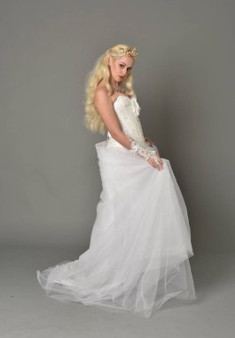 tam uzunlukta portre sarışın kız beyaz fantezi elbise giyiyor. yan profil, gri studio arka plan ayakta poz.