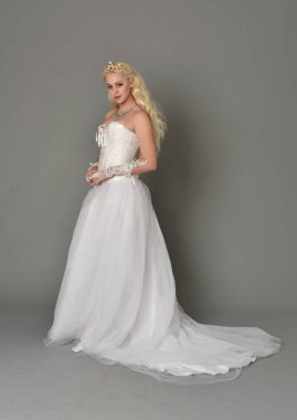 tam uzunlukta portre sarışın kız beyaz fantezi elbise giyiyor. yan profil, gri studio arka plan ayakta poz.