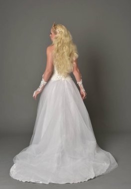 tam uzunlukta portre sarışın kız beyaz cüppe, kameranın arka ayakta pozuyla giyiyor. gri studio arka plan.