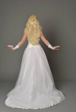 tam uzunlukta portre sarışın kız beyaz cüppe, kameranın arka ayakta pozuyla giyiyor. gri studio arka plan.