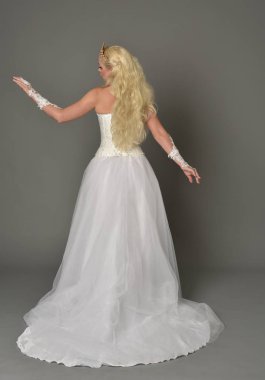 tam uzunlukta portre sarışın kız beyaz cüppe, kameranın arka ayakta pozuyla giyiyor. gri studio arka plan.